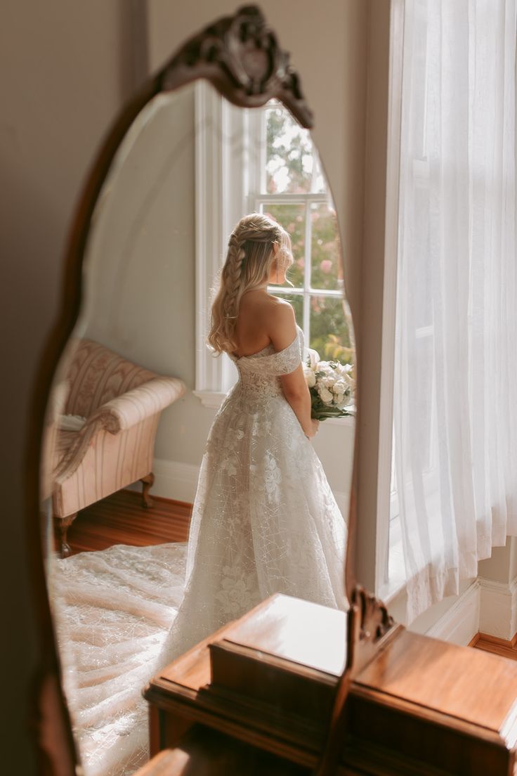 a woman standing in front of a mirror wearing a wedding dress