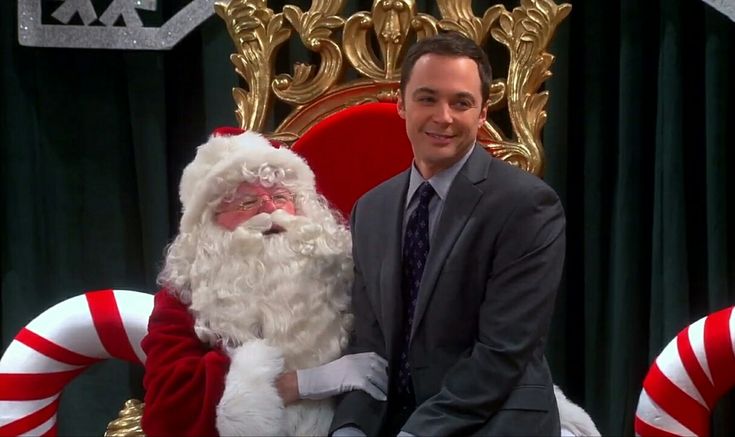 a man in a suit and tie sitting next to a santa clause