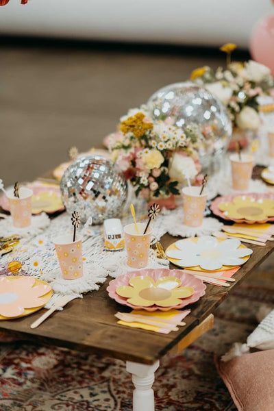 the table is set with pink and gold plates, silver balls, and flowers in vases