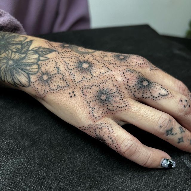 a person with black dots on their hand and tattoo designs on his left hand, sitting in a chair