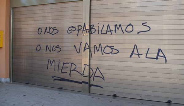 graffiti written on the side of a closed garage door in spanish and latin writing is shown