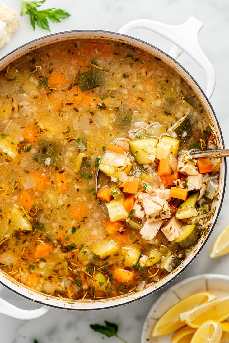 a pot filled with chicken and vegetable soup on top of a table next to sliced lemons