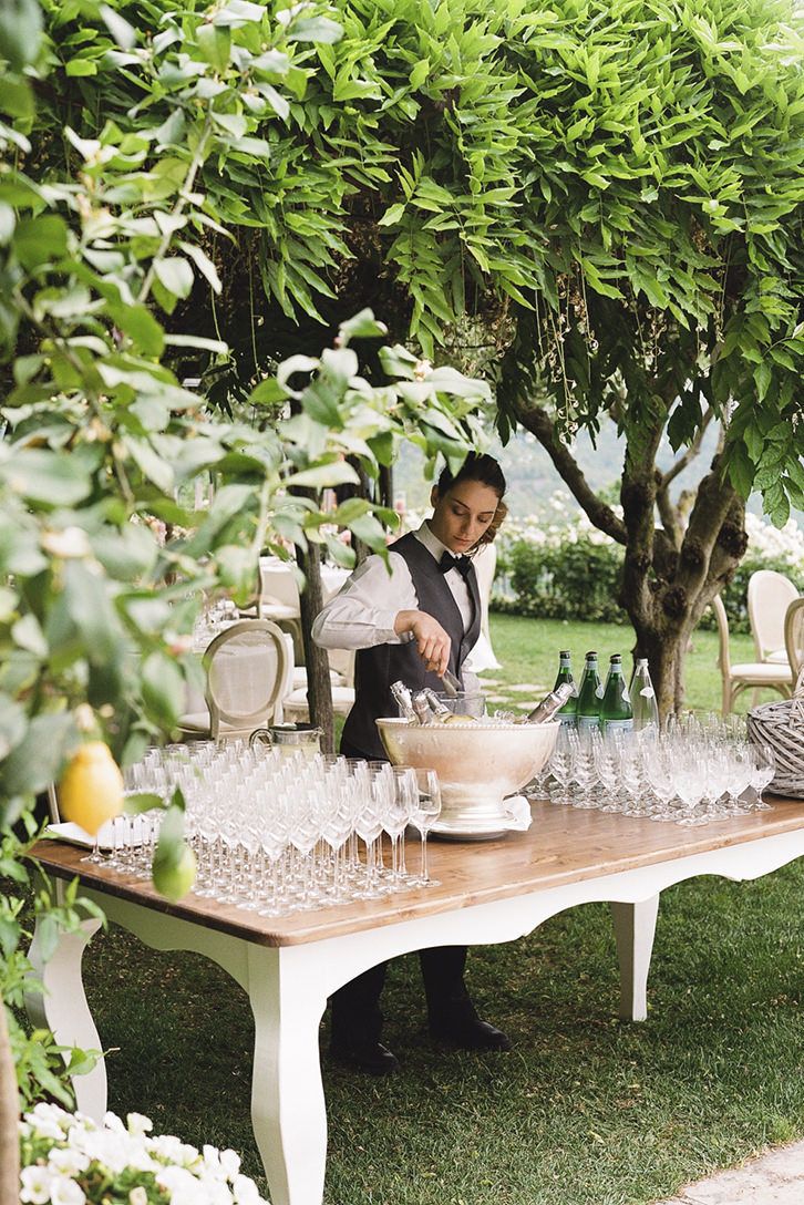 a man sitting at a table with wine glasses and bottles on it, surrounded by greenery