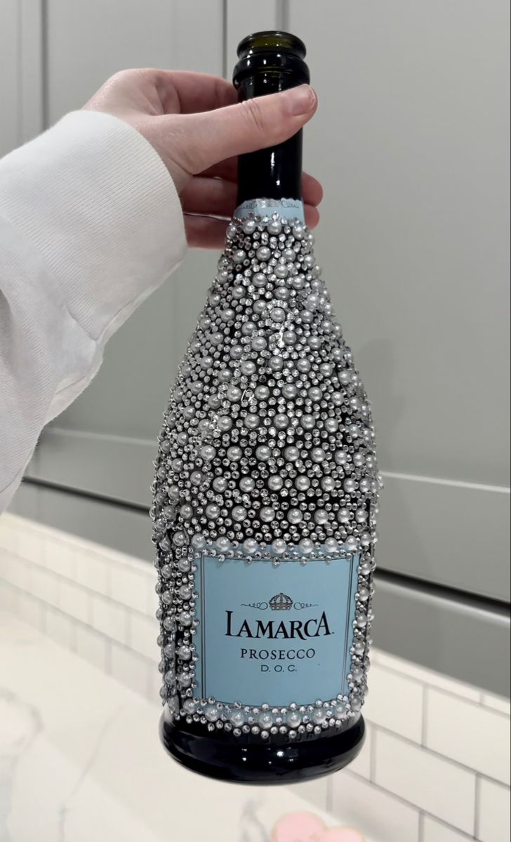 a person holding a bottle of wine in front of a sink with white tiles on it