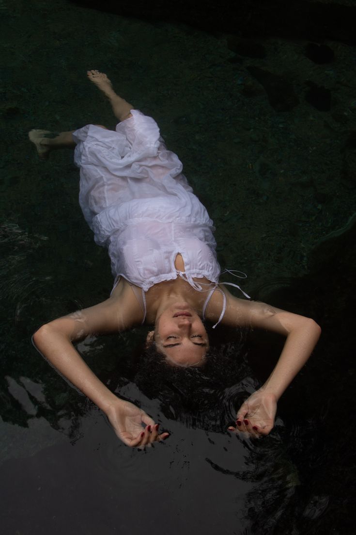 a woman is floating in the water wearing a white dress and holding her head up