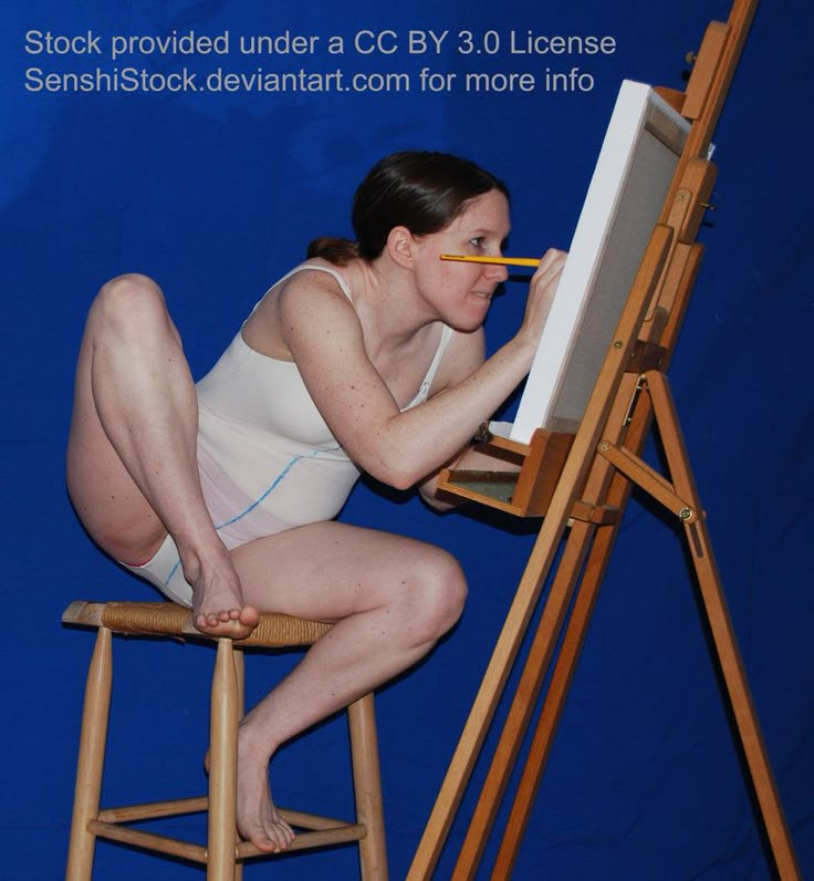 a woman sitting on a chair in front of an easel and holding a pencil