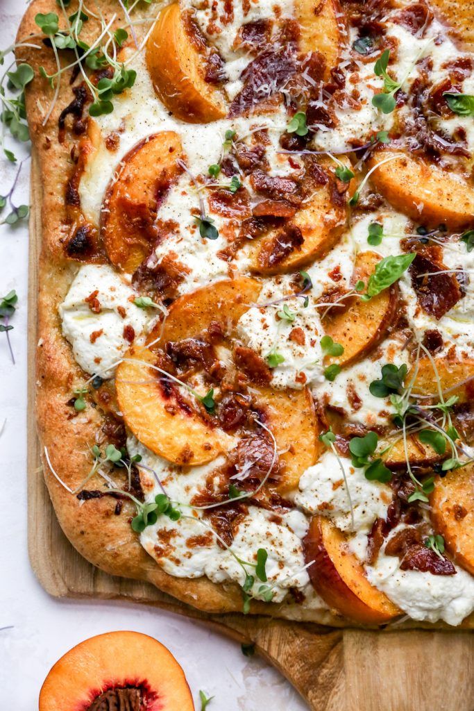 a pizza topped with lots of toppings on top of a wooden cutting board next to sliced peaches