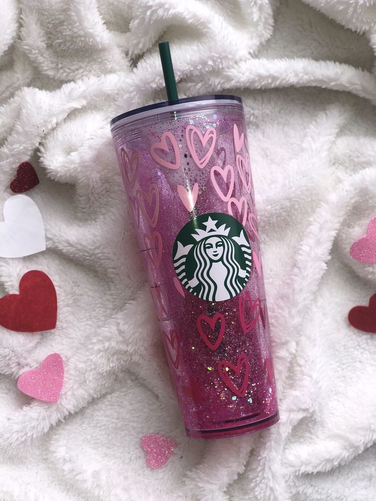 a pink starbucks cup sitting on top of a white blanket with hearts and confetti