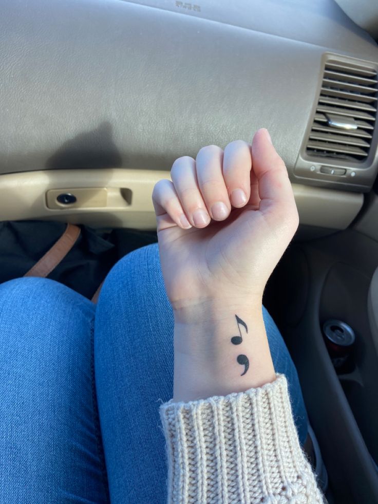 a woman's wrist with a musical note tattoo on her left hand, sitting in a car