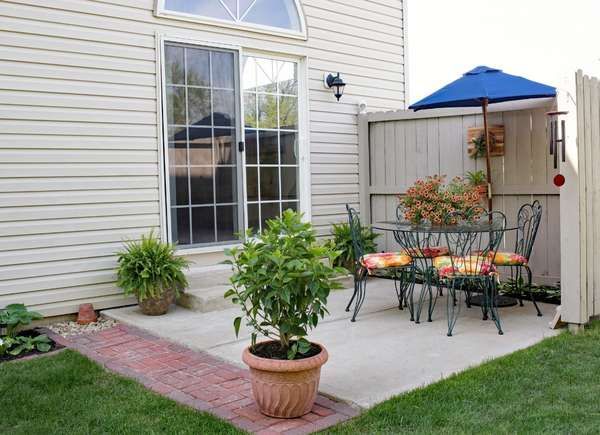 a patio with table, chairs and an umbrella in the back yard on a sunny day