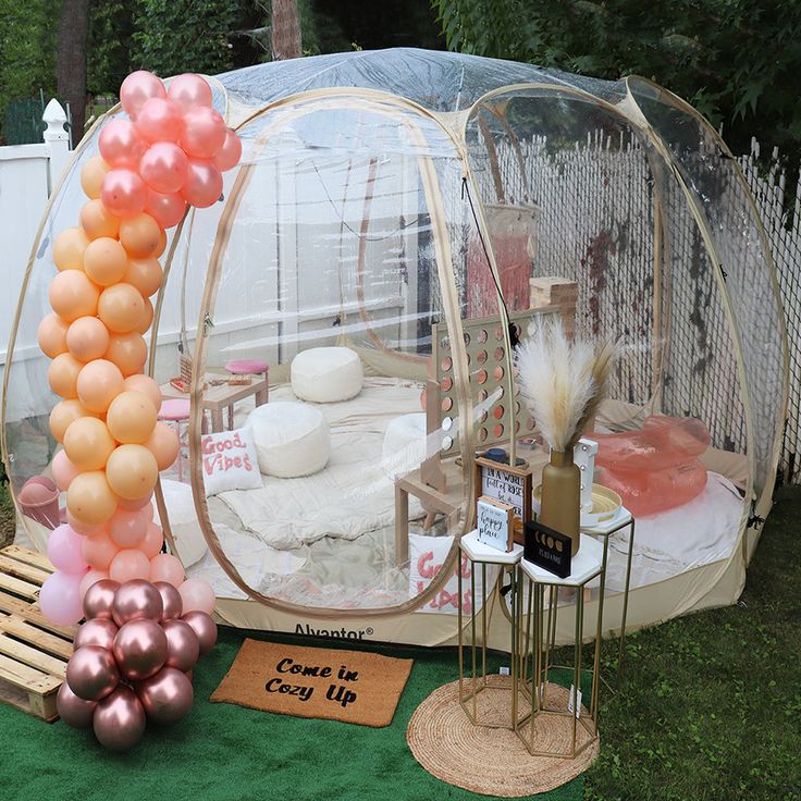 an outdoor party setup with balloons and cake in a bubble tent, on the grass