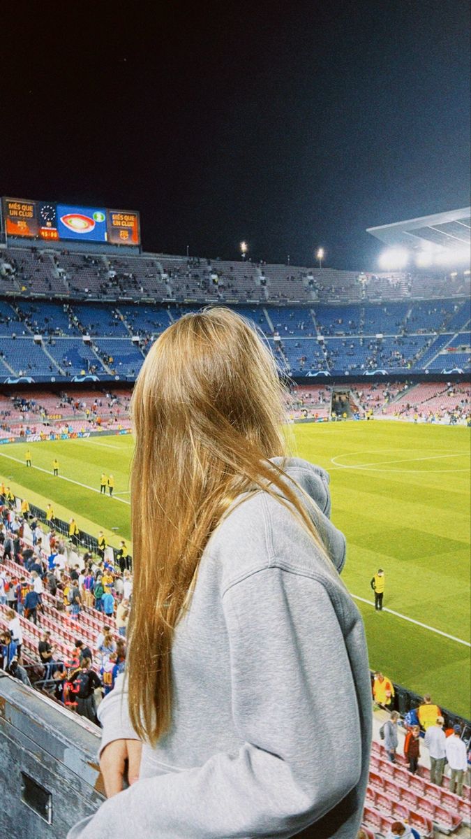 a woman sitting in the stands at a soccer game looking out over the field and into the crowd