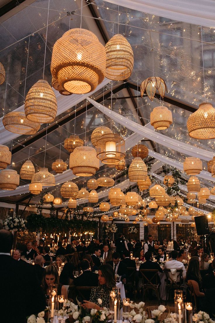 a group of people sitting at tables under lights and chandeliers in a tent