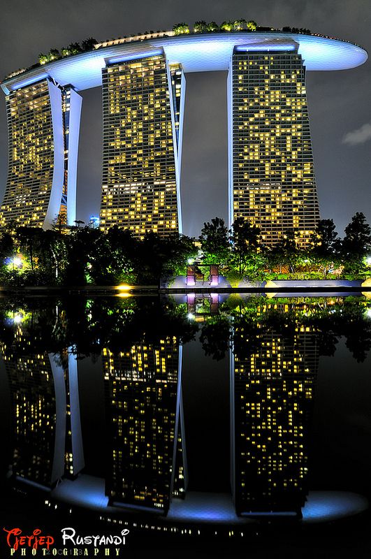 an image of a city at night with lights on the buildings and water reflecting in the foreground