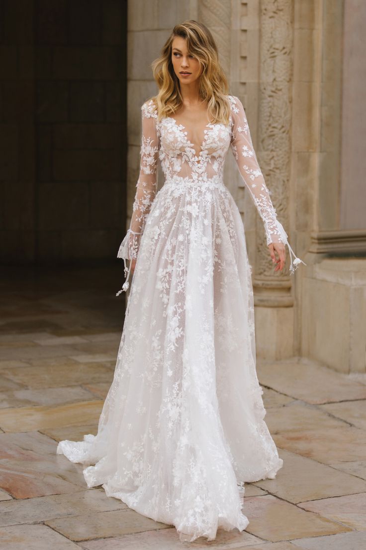 a woman in a white wedding dress standing on a stone floor with her arms outstretched