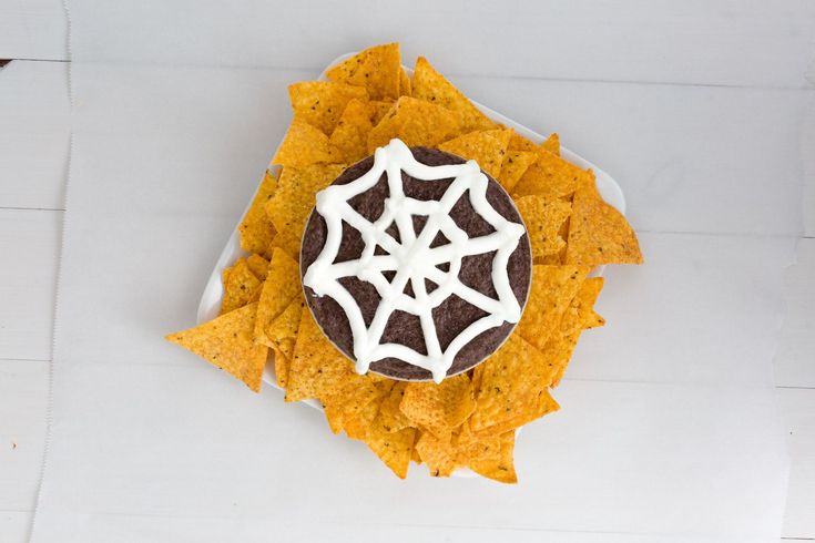 a spider web on top of tortilla chips with sour cream and black pepper