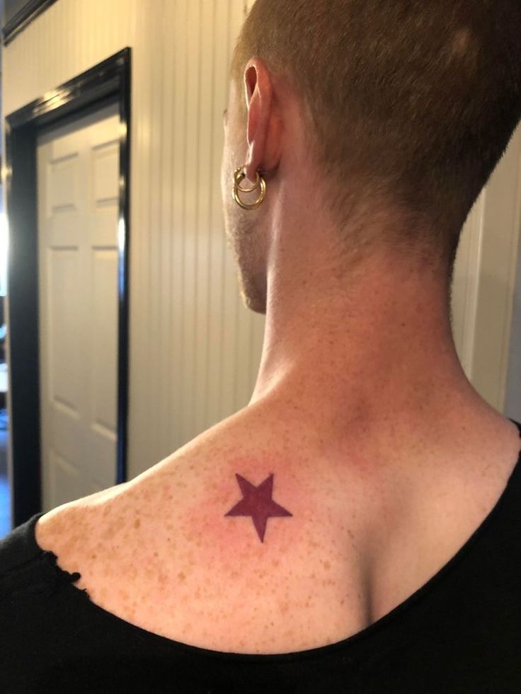 a man with a small star tattoo on his back shoulder and neck, standing in front of a door