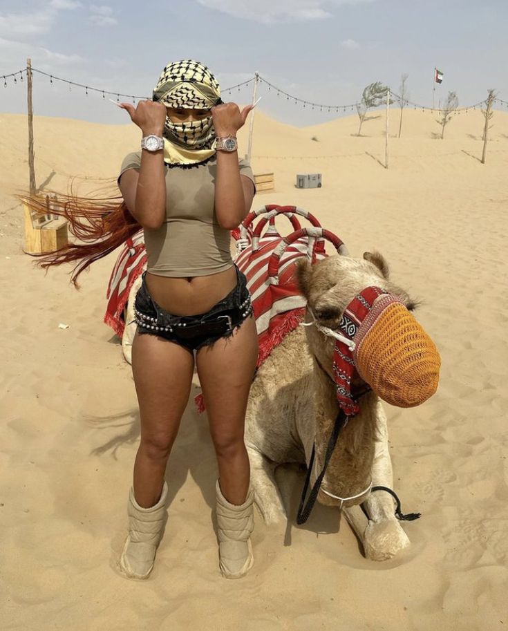 a woman in short shorts standing next to a camel