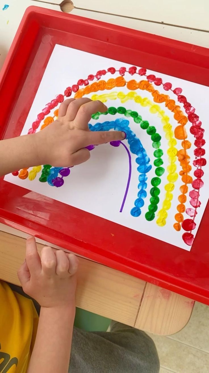 a young boy is painting with colored beads on a tray in front of his table