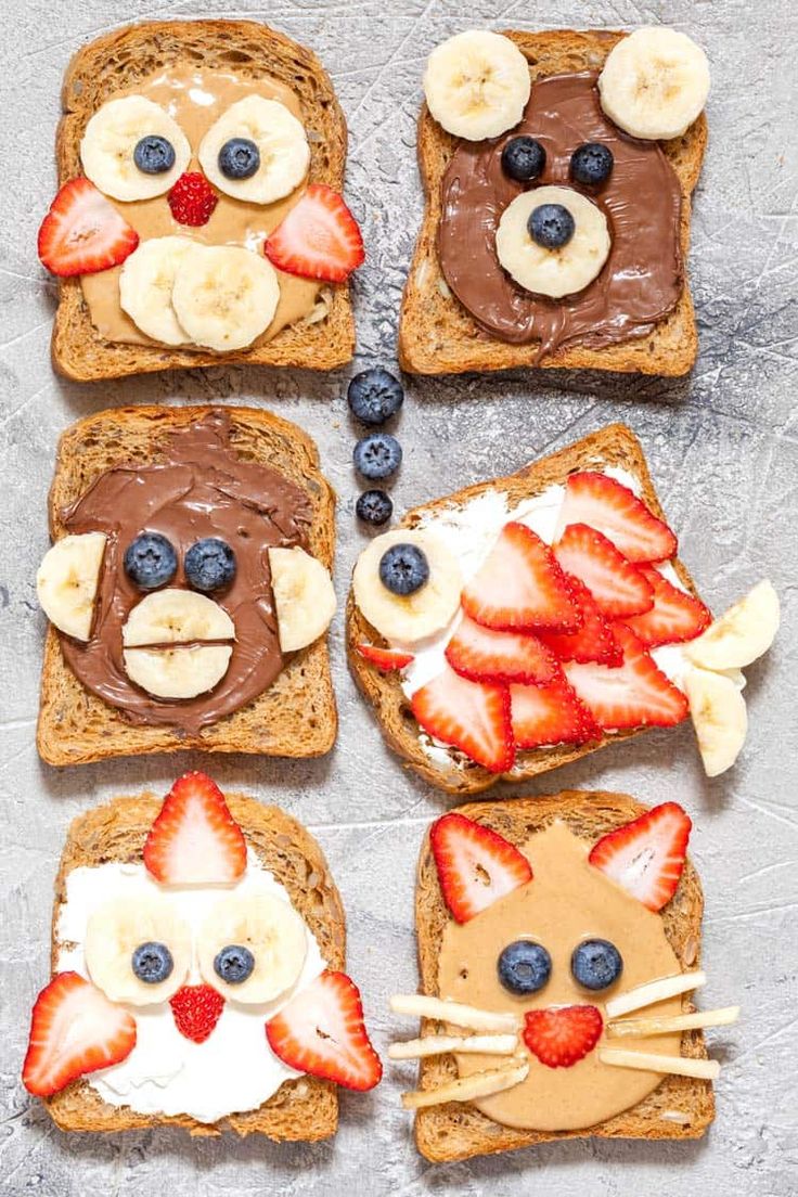 four slices of toast with fruit and chocolate on them, each decorated like a cat