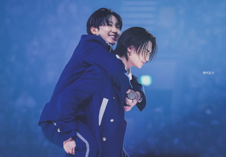 two young men standing next to each other in front of a blue background with lights