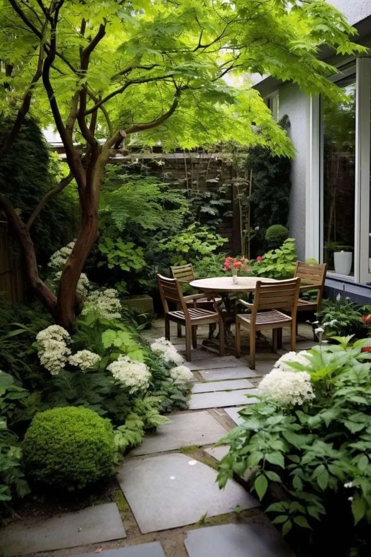 a table and chairs in the middle of a garden with trees, bushes and flowers