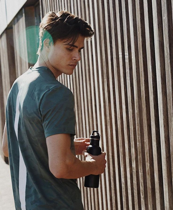 a young man standing next to a wall holding a bottle and looking at his cell phone