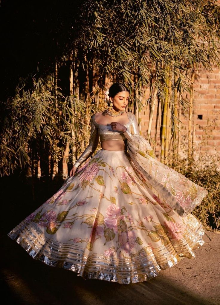 a woman in a white and pink lehenga is posing for the camera with her hands on her hips