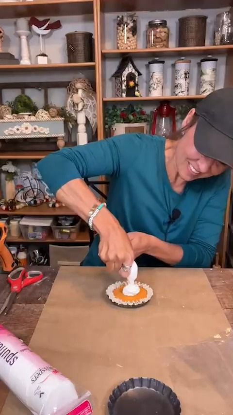 a woman in a blue shirt and hat is making a small cake with icing