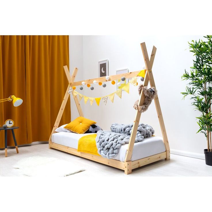 a child's bed with a wooden frame and yellow pillows on the bottom, next to a potted plant