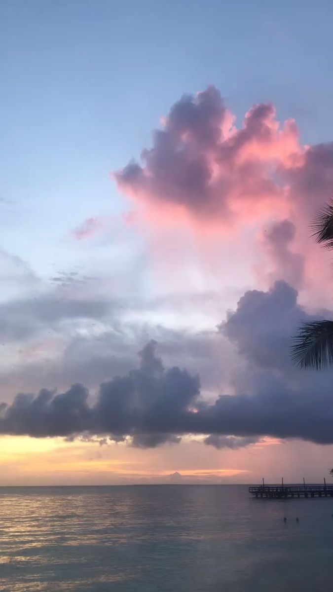 the sun is setting over the ocean with clouds in the sky and palm trees on the beach