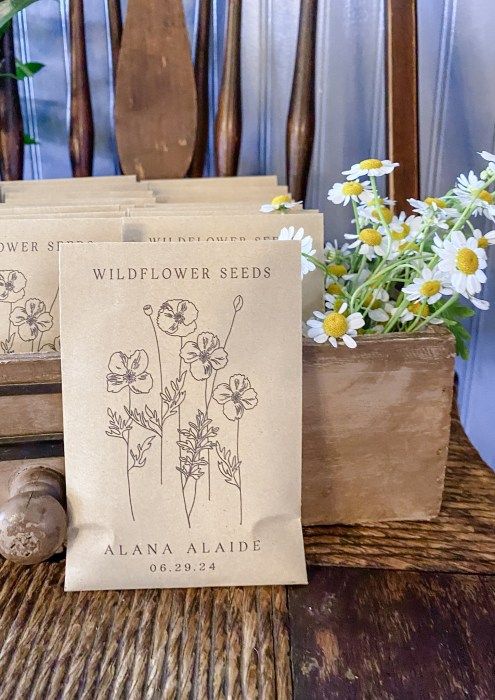 two bags of wildflower seeds sitting on top of a wooden table next to flowers