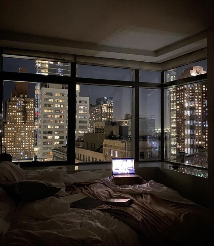 a laptop computer sitting on top of a bed in front of a window at night