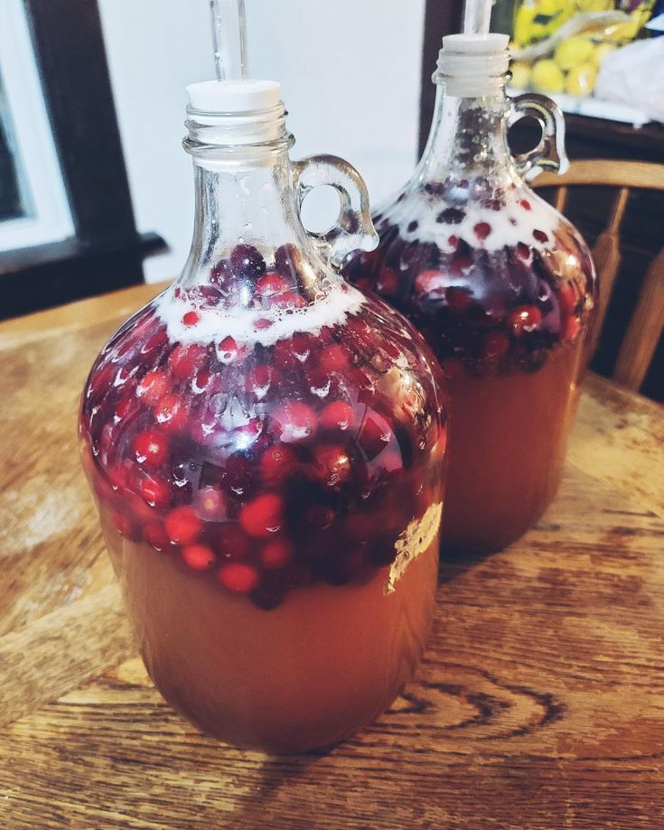 two glass jugs filled with liquid sitting on top of a wooden table