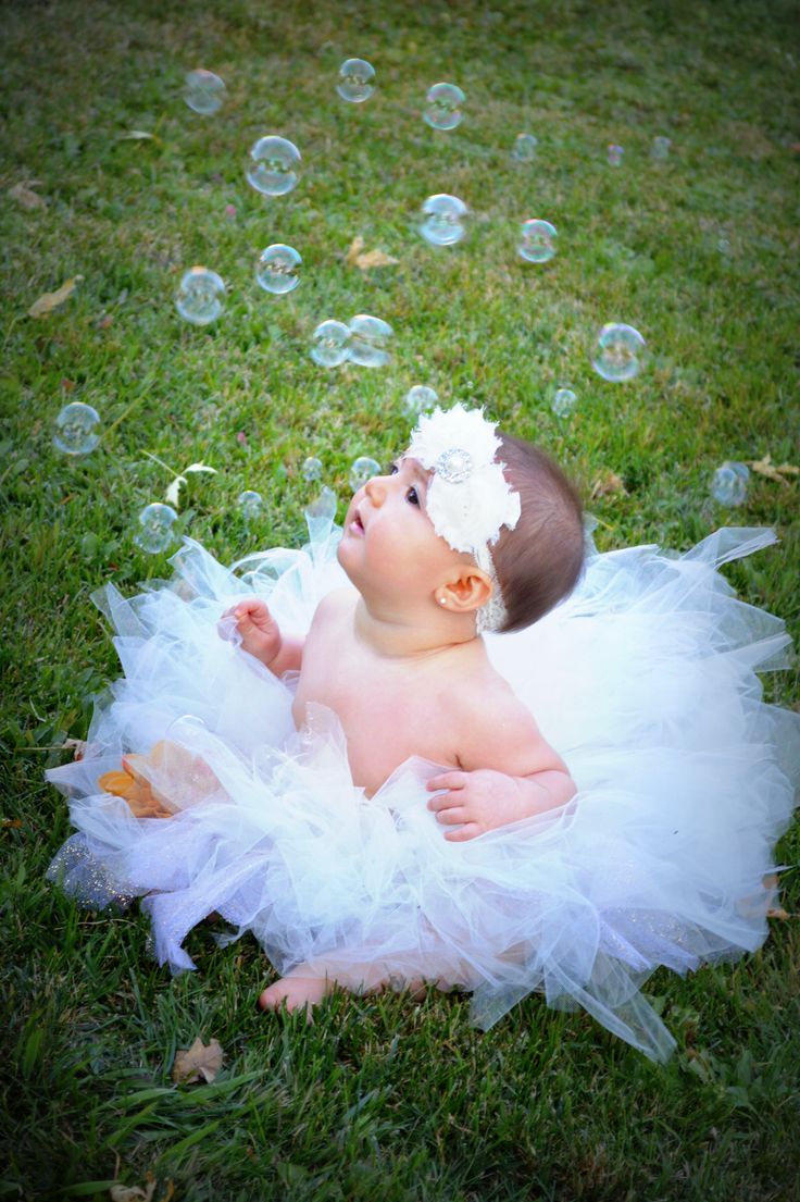 a baby wearing a white tutu laying on the grass with bubbles in the air