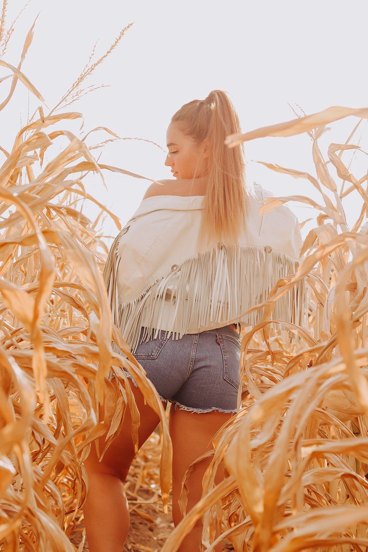 a woman standing in the middle of a corn field with her hands on her hips