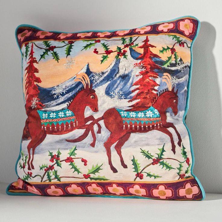 a decorative pillow with two horses running through the snow covered mountains and pine trees on it