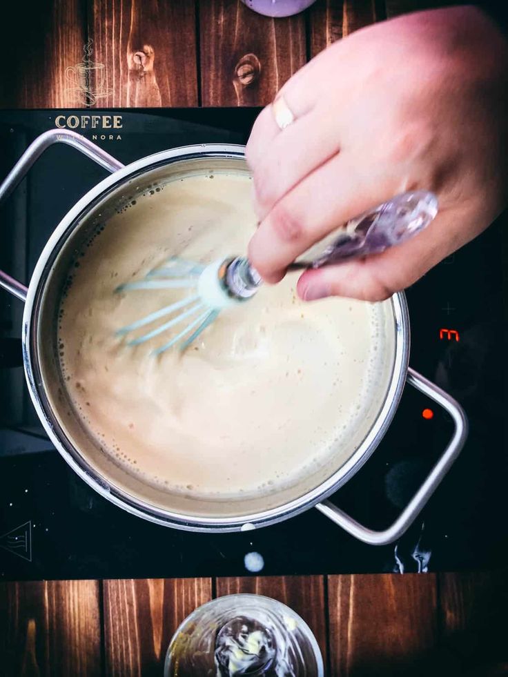 someone is stirring something in a saucepan on the stove with a whisk