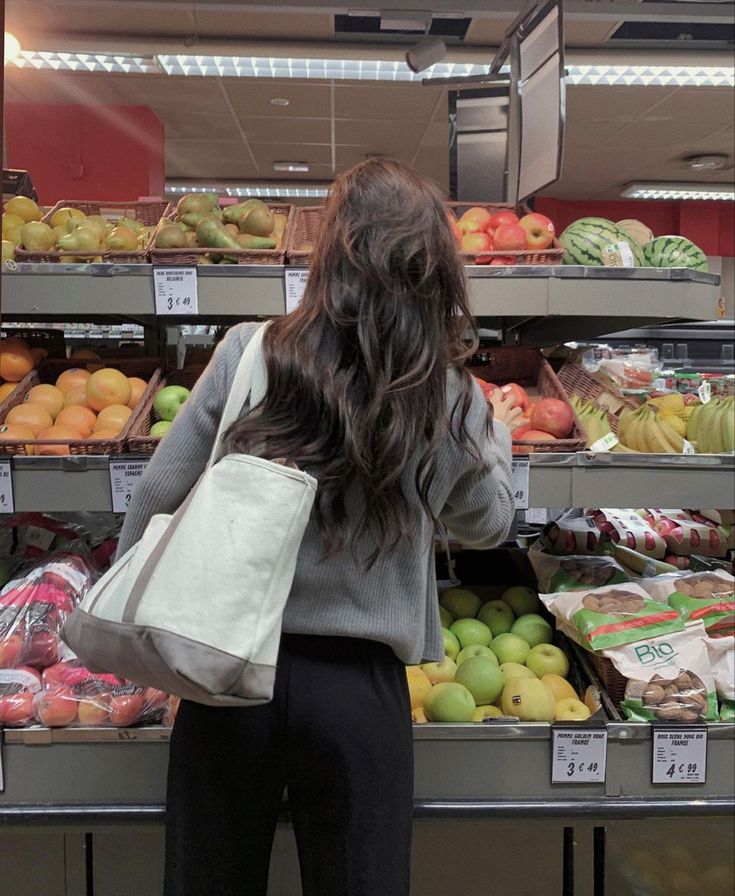 a woman standing in front of a display of fruits and vegetables at a grocery store