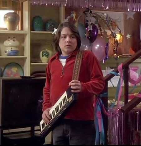 a young boy holding a musical instrument in front of a shelf with balloons and streamers