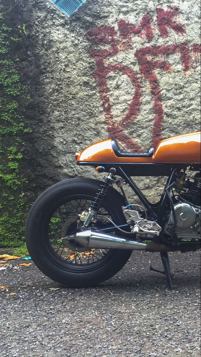 an orange and black motorcycle parked in front of a wall with graffiti written on it