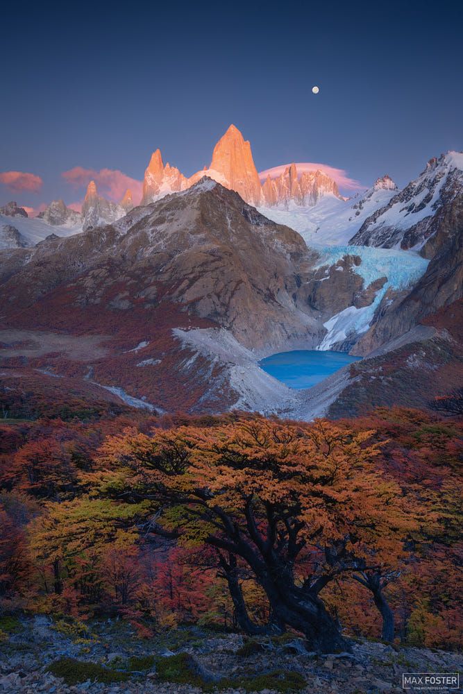 the mountains are covered in snow and trees with orange leaves on them, as the sun sets