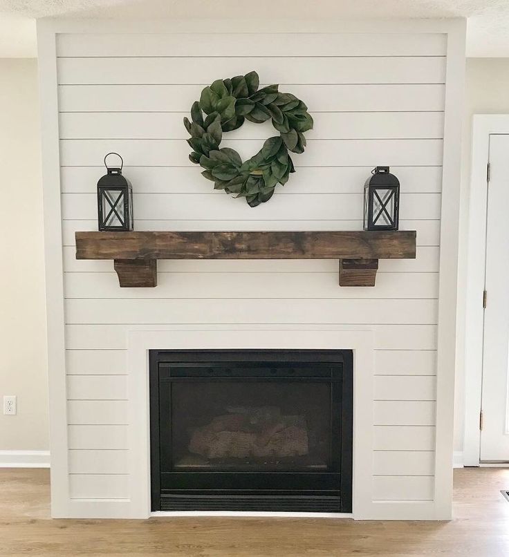 a fireplace with a wreath on the mantle and two lanterns hanging from the mantel