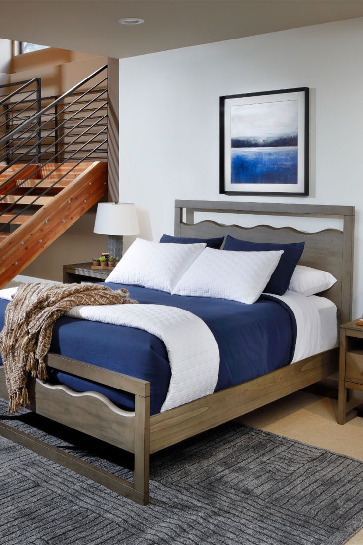 a bed with blue sheets and white pillows in a bedroom next to a stair case