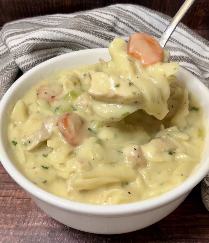 a white bowl filled with pasta and meat on top of a wooden table next to a napkin