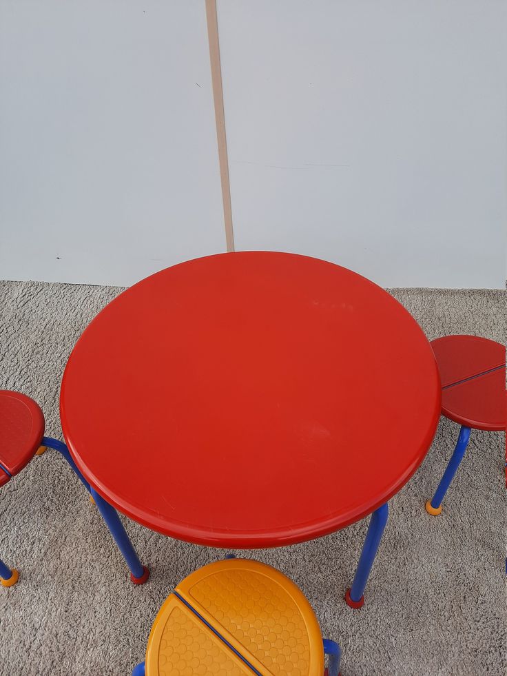 a red table with four chairs around it on carpeted floor next to white wall