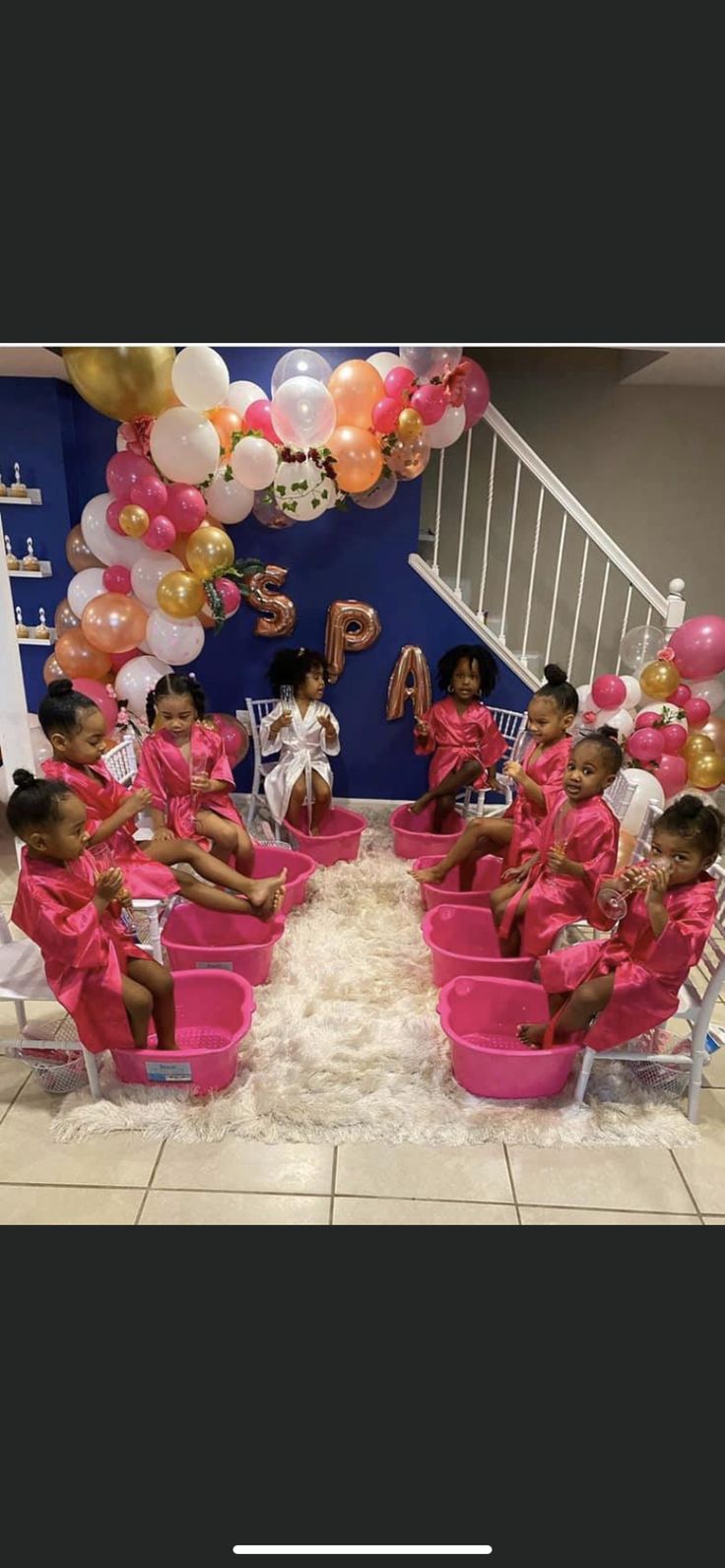 some kids are sitting in pink buckets with balloons and streamers on the wall