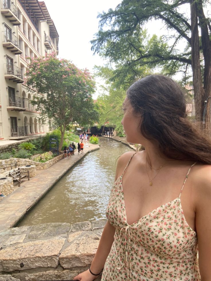 One girl standing by bridge overlooking water. She’s in a spaghetti strap floral dress. Long brown hair. Strap Dress Outfit, San Antonio Riverwalk, Long Brown Hair, Long Wavy Hair, Instagram Pose, Brown Hair Colors, Strap Dress, Spaghetti Strap Dresses, San Antonio