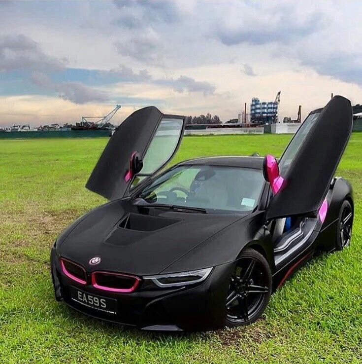 a black sports car with its doors open on the grass in front of some buildings