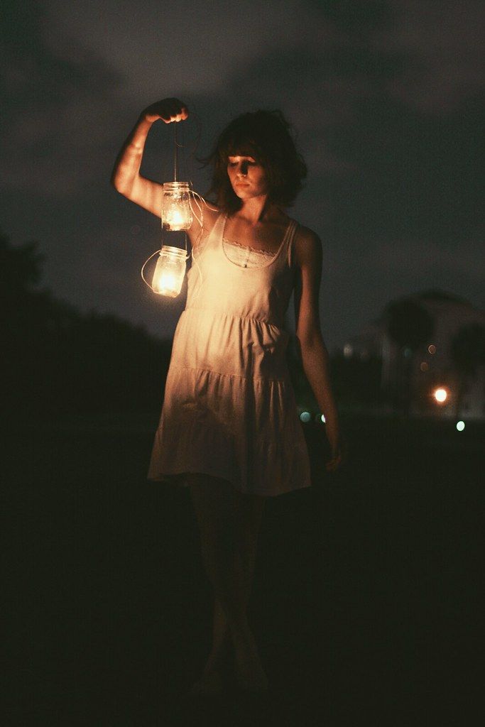 a woman holding a lantern in her hand at night with the light shining on her arm